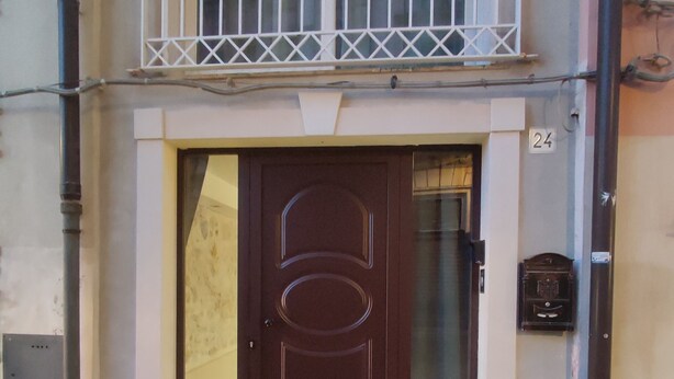 L’entrée d’un immeuble se distingue par une porte de couleur marron foncé, un petit balcon doté de balustrades blanches et le chiffre « 24 » peint sur le mur.