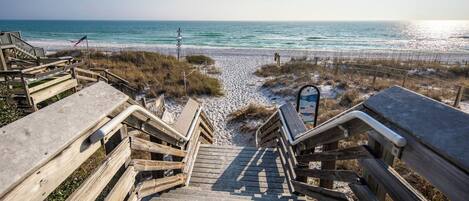 A wooden staircase leading to a beach with a sandy path and a signboard.