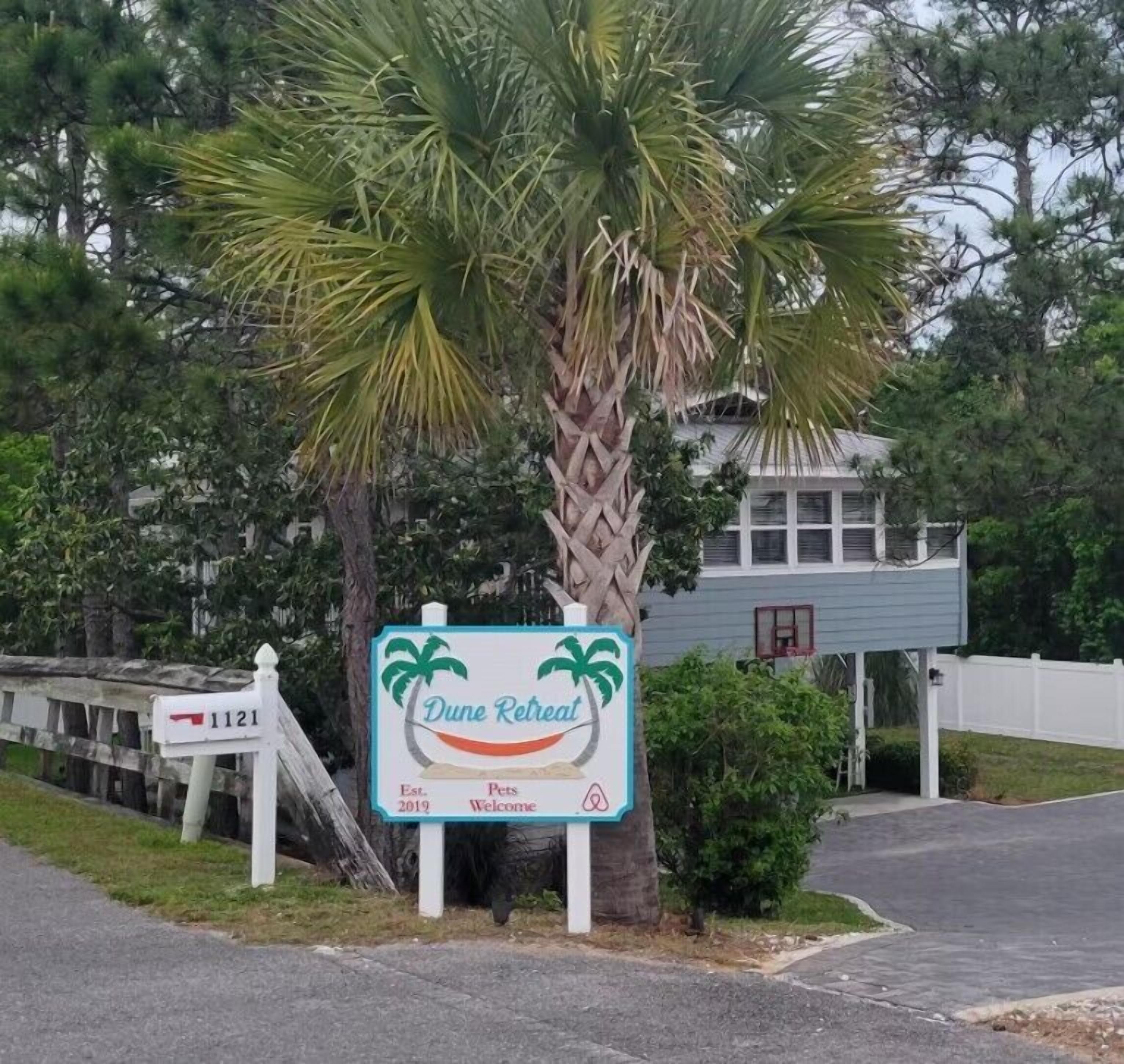 A sign for 'Dune Retreat' with a palm tree and a house in the background.