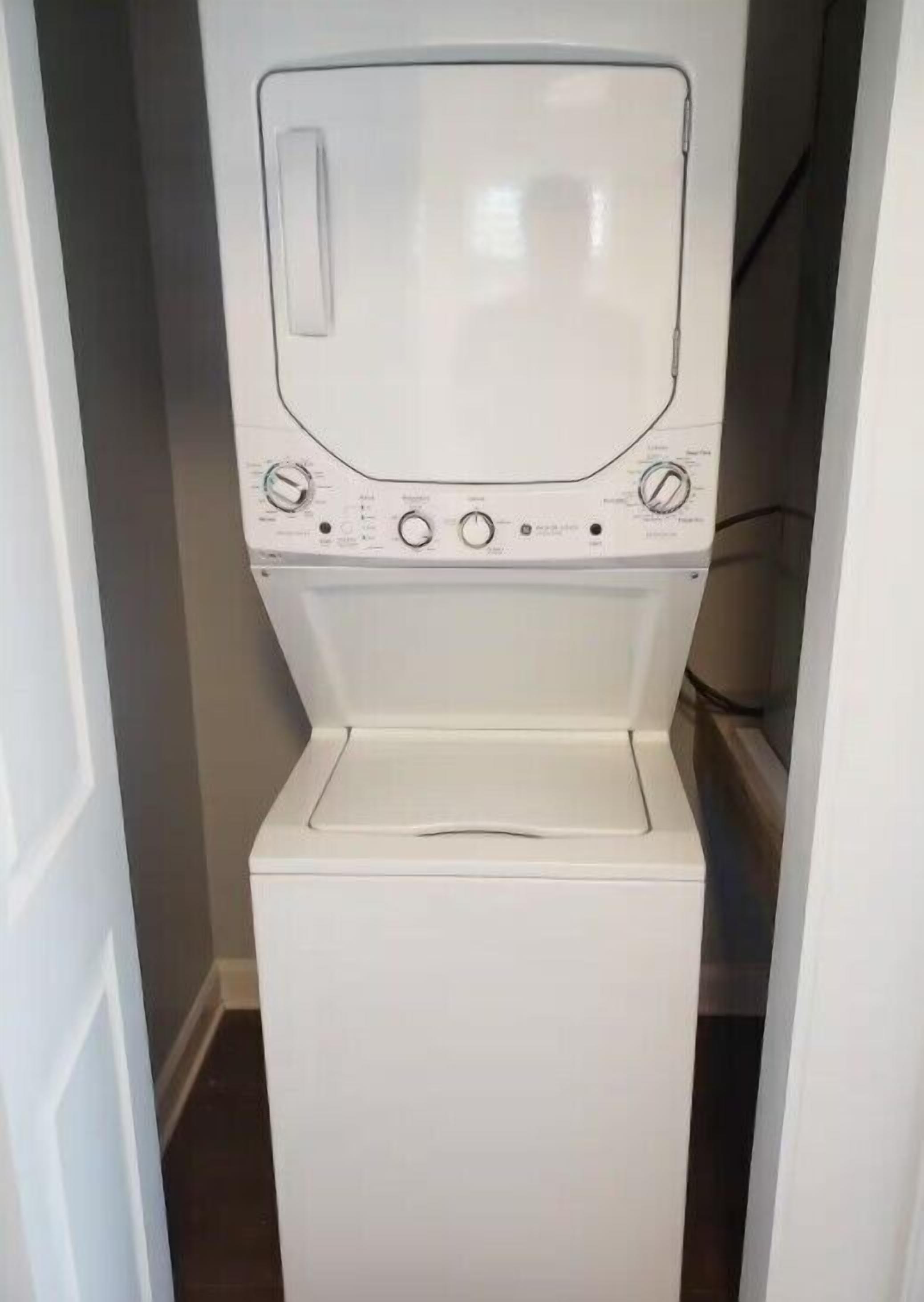 A compact, white, front-loading washing machine in a narrow hallway.