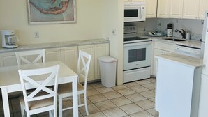 A kitchen with white cabinets, a dining table with chairs, a coffee maker, a microwave, and an oven.