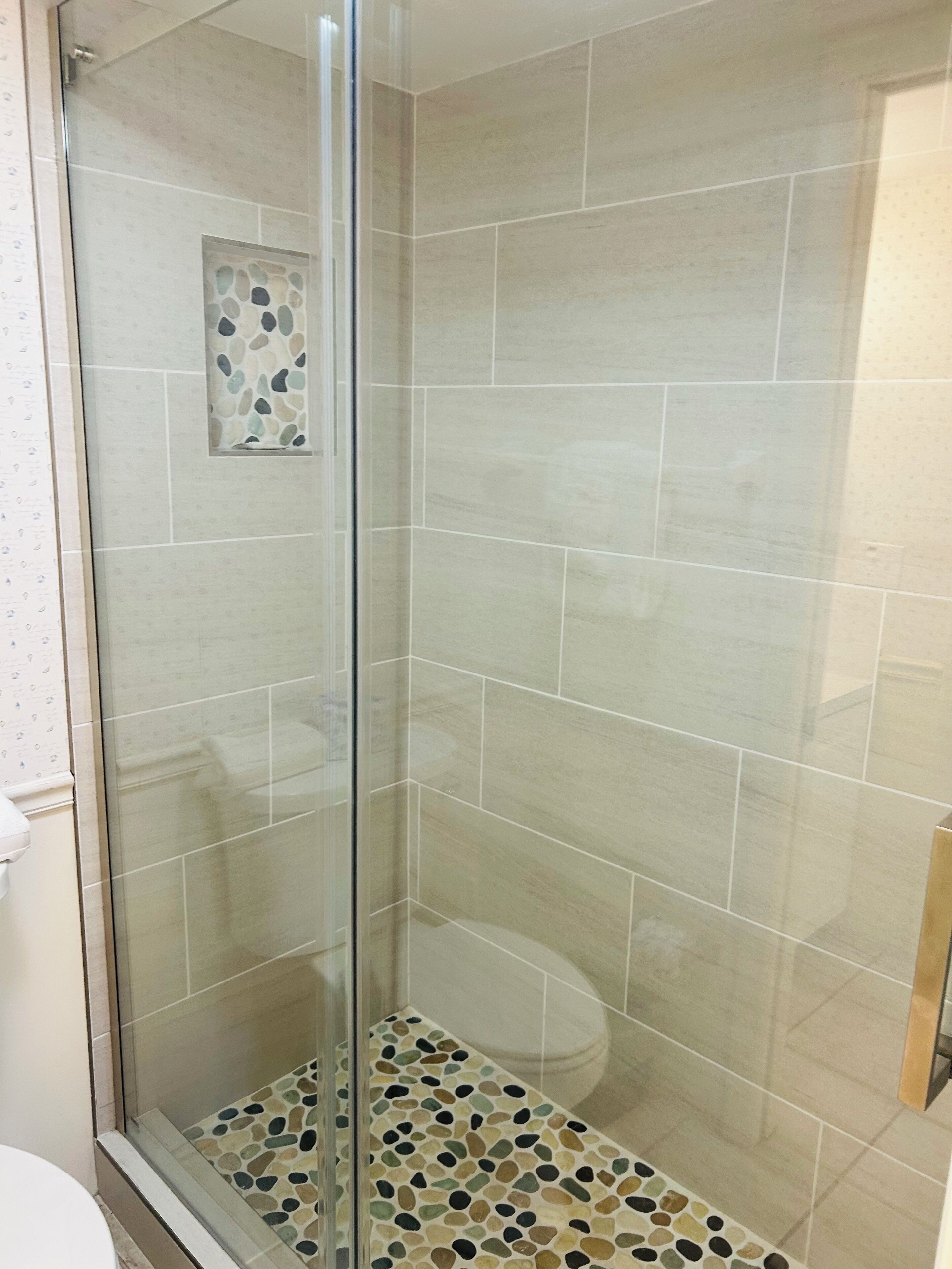 Een douche met een glazen deur en een vloer met een patroon van kiezels.