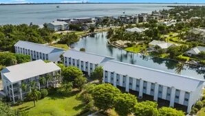 A modern hotel with a pool, surrounded by lush greenery and a view of the sea.