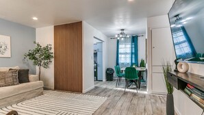 A modern living room with a sofa, a wooden partition, and a dining area with green chairs.