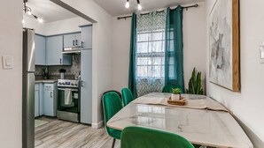 A compact kitchen with modern appliances, a dining area with a marble table, and a view of the outside through patterned curtains.