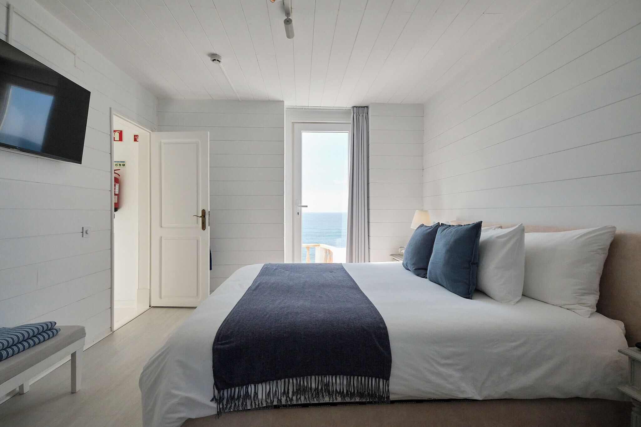 Une chambre avec un lit, un banc, une télévision et une vue sur la mer.
