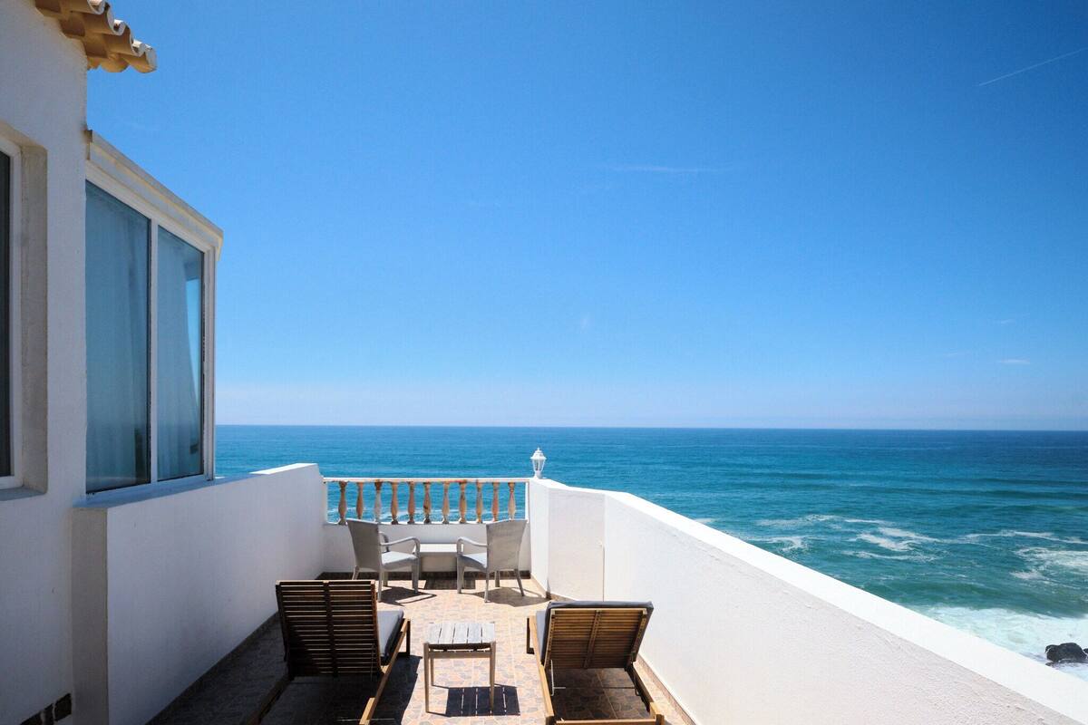 Ein Balkon mit Blick auf das Meer, ein Tisch, Stühle und ein kleiner Beistelltisch.