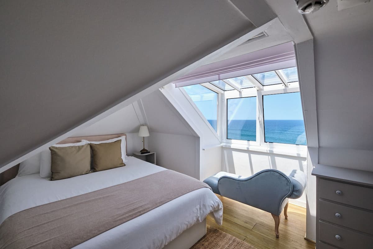 Ein Schlafzimmer mit Bett, Nachttisch, Lampe und Meerblick durch ein Oberlicht.