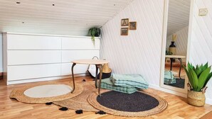 Une pièce avec un plancher en bois, une table ronde avec une chaise, un petit tapis, un miroir et une plante en pot.