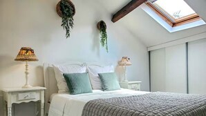 Une chambre à coucher avec un lit, deux tables de chevet, une lucarne et des plantes suspendues.
