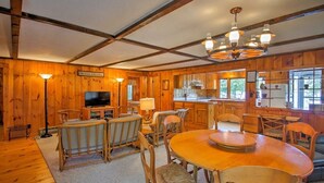 A wooden cabin interior with a dining area, kitchen, and a television. - Stonedam Cottage on the shores of Lake Winni (Meredith)