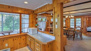A wooden cabin interior with a kitchen area, dining table, and chairs. - Stonedam Cottage on the shores of Lake Winni (Meredith)