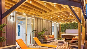 Une terrasse extérieure avec des poutres en bois, des fauteuils de jardin orange, une table ronde et un jacuzzi.