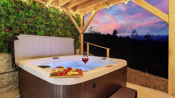 Un bain à remous doté d’une terrasse en bois, entouré d’un mur végétal luxuriant et offrant une vue imprenable sur le ciel au crépuscule.