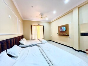 A hotel room with two beds, a ceiling fan, a TV mounted on the wall, and a window with curtains.