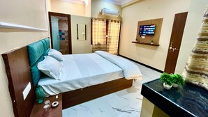 A hotel room with a bed, a small desk, a TV, and an air conditioning unit. - Raghav ji home stay (Orchha)