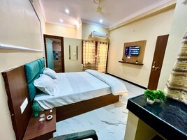 A hotel room with a bed, a small desk, a TV, and an air conditioning unit.