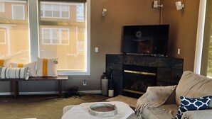 A living room with a sofa, a coffee table, a lamp, a fireplace, and a television.