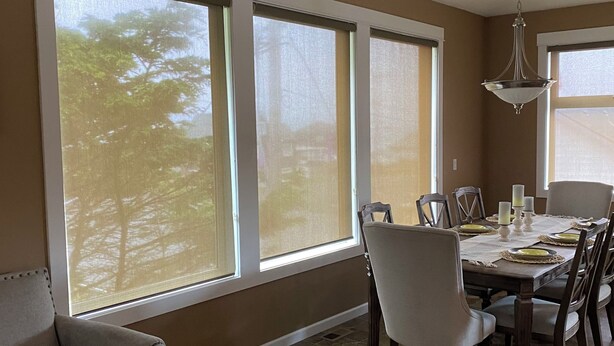 A dining area with a table set for four, large windows, a chandelier, and a sofa.