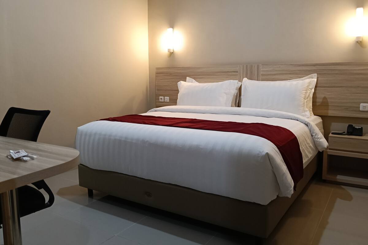 Une chambre d’hôtel avec un lit, un bureau et deux lampes fixées au mur.