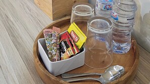 A wooden tray with snacks, water bottles, a kettle, and a tissue box on a wooden table. - Sunflower Hotel Syariah Near Juanda (Sidoarjo)