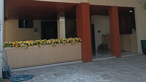 A covered outdoor area with a reception desk, a flower display, and a brick-paved floor. - Sunflower Hotel Syariah Near Juanda (Sidoarjo)