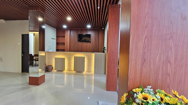 A reception area with a wooden reception desk, a flat-screen TV mounted on the wall, and a potted plant. - Sunflower Hotel Syariah Near Juanda (Sidoarjo)