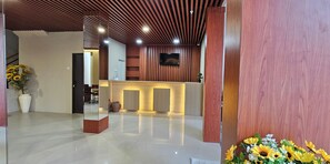 A reception area with a wooden reception desk, a flat-screen TV mounted on the wall, and a potted plant. - Sunflower Hotel Syariah Near Juanda (Sidoarjo)