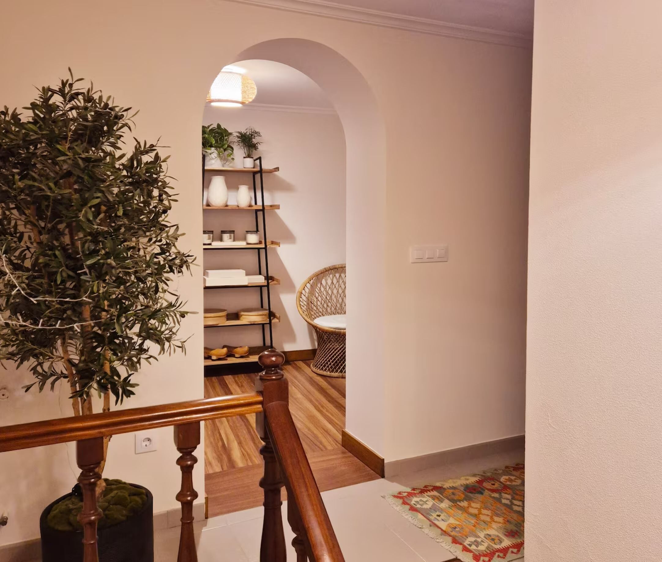 A staircase with a wooden handrail, a potted plant, a wicker chair, and a shelf with decorative items.
