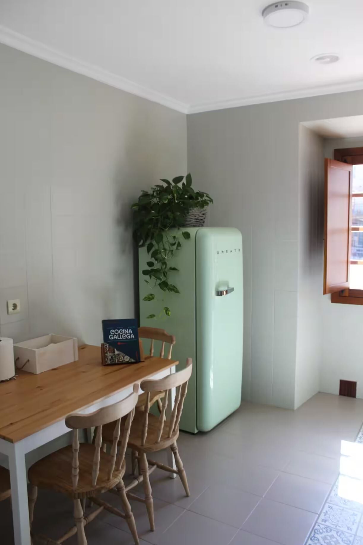 A kitchen with a dining table and chairs, a light green refrigerator, and a potted plant on top.