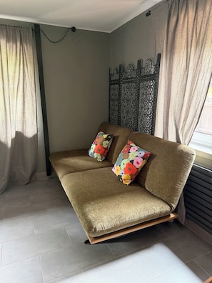 A room with a sofa, two patterned cushions, a decorative wall panel, and a window with curtains. - Two Brothers Inn (Pertisau)