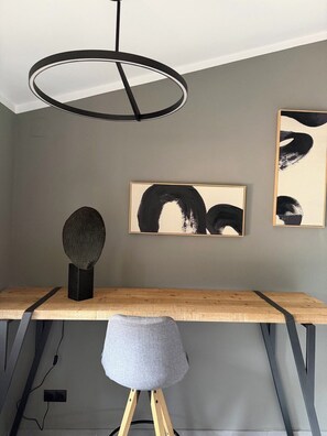 A modern room with a wooden desk, a grey chair, a pendant light, and abstract art on the wall.