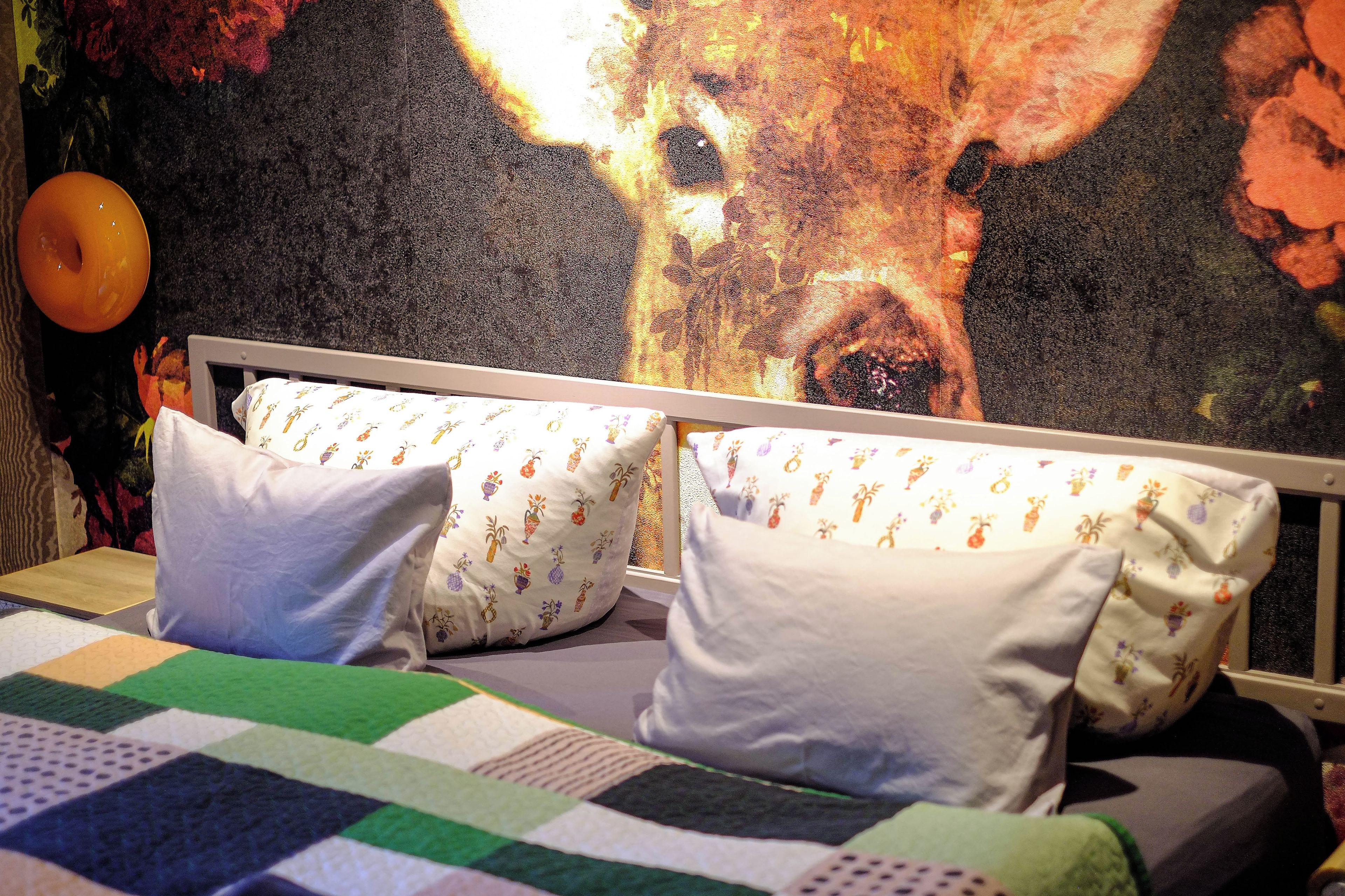 A bed with a quilt, pillows, and a headboard against a wall with a floral mural.