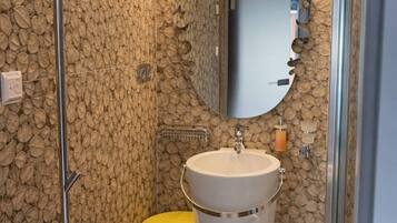 Un baño con pared de piedra, un lavamanos blanco, un taburete amarillo y una cabina de ducha de cristal.
