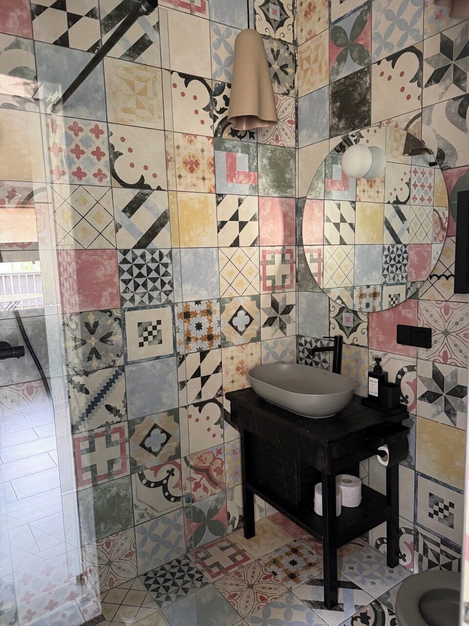 Un bagno con lavandino, WC e specchio. Le pareti sono rivestite da diversi motivi geometrici.