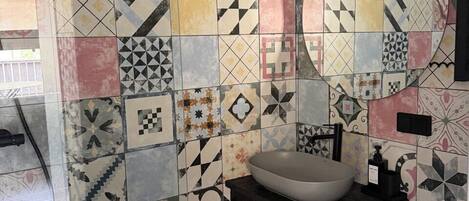 Un baño con lavamanos, inodoro y espejo. Las paredes están cubiertas de distintos diseños geométricos.