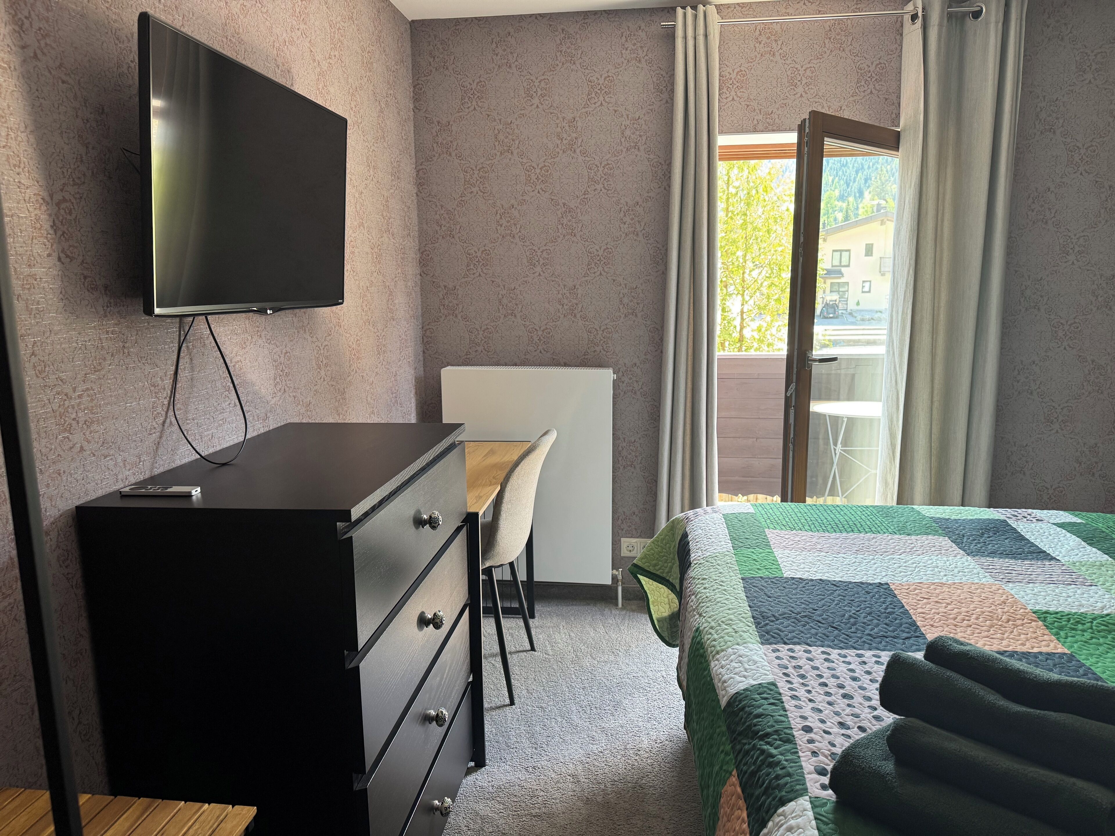 A hotel room with a bed, a desk, a chair, a television, and a window with curtains.