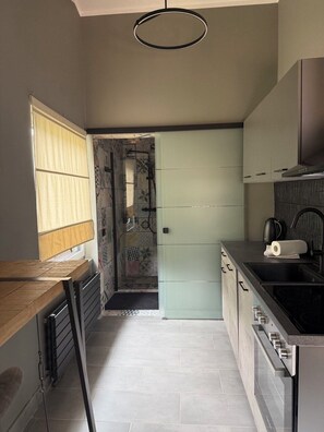 A compact kitchen with a built-in oven, a sink, and a window with blinds.