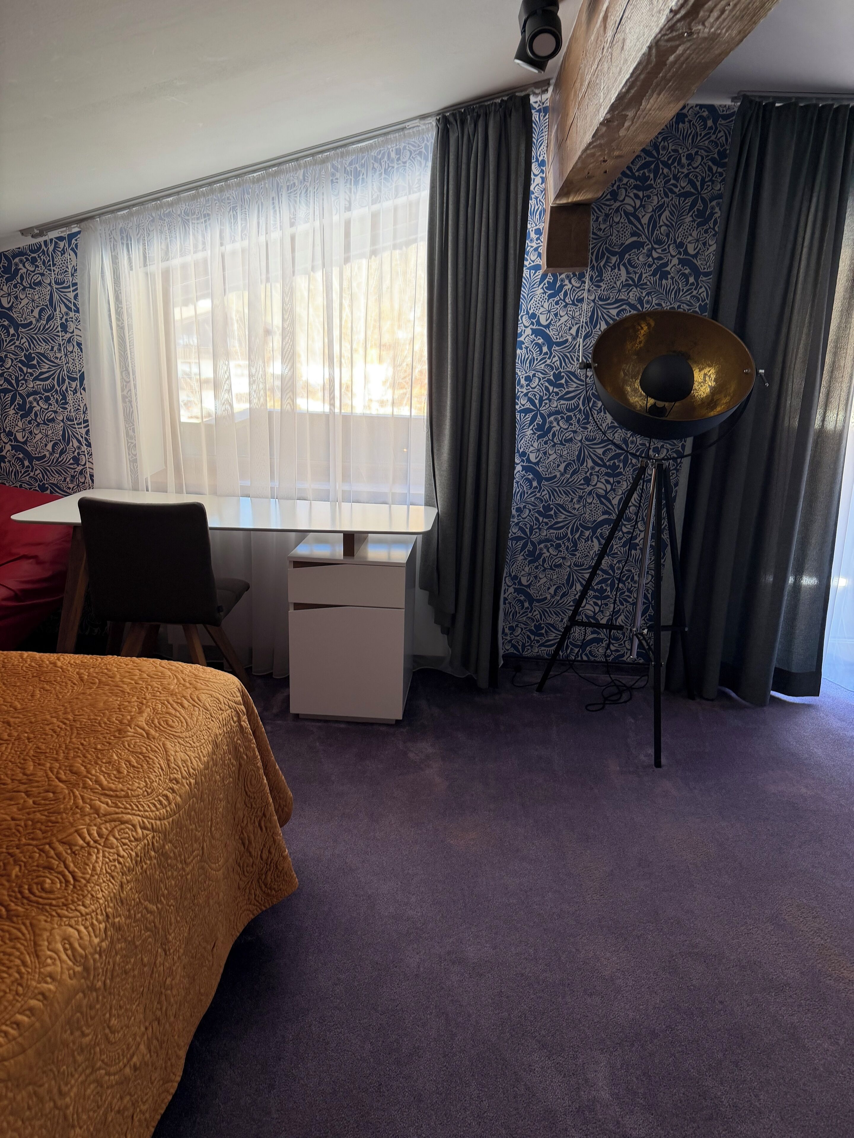 Une chambre d’hôtel comprenant un lit, un bureau, une chaise, une armoire et une lampe sur pied.