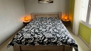 A bedroom with a bed, a hanging light fixture, a bedside table, and a window with curtains.