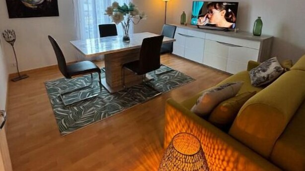 A modern living room with a sofa, a dining area with a table and chairs, a TV, and a unique patterned floor lamp.