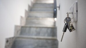 Sleutels hangend aan een sleutelgat dat aan de muur bevestigd is, met een trap op de achtergrond.