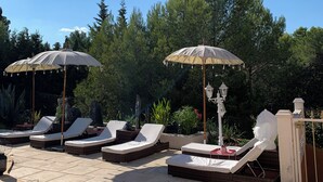 Zona de piscina amb gandules i ombrelles, una piscina i una estàtua.