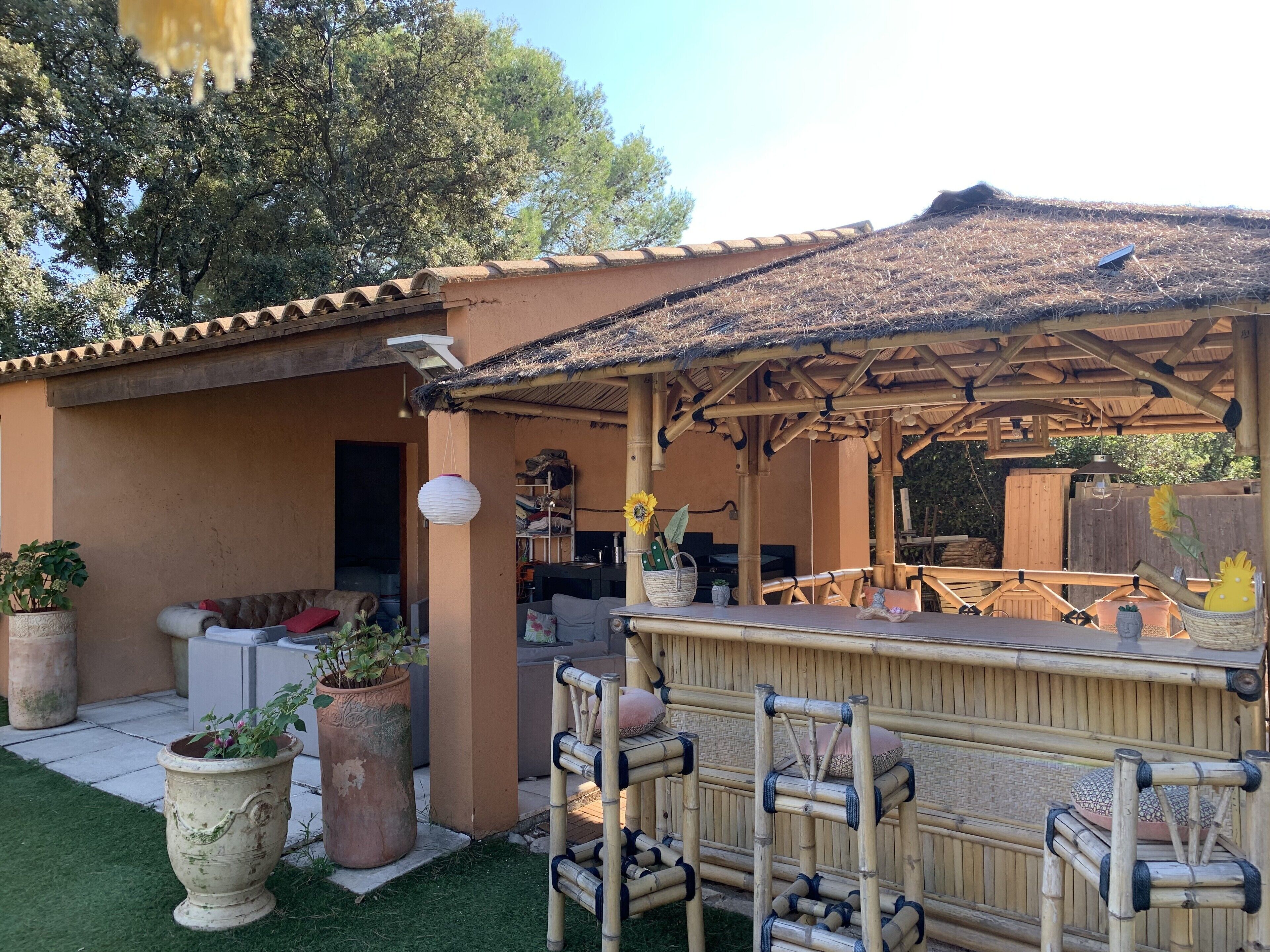 Een overdekt terras met een bamboestructuur, een bar en potplanten.
