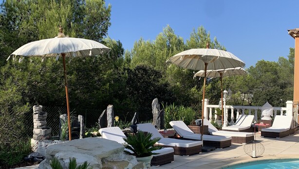 Zona de piscina amb gandules, ombrel·les i una paret de pedra.