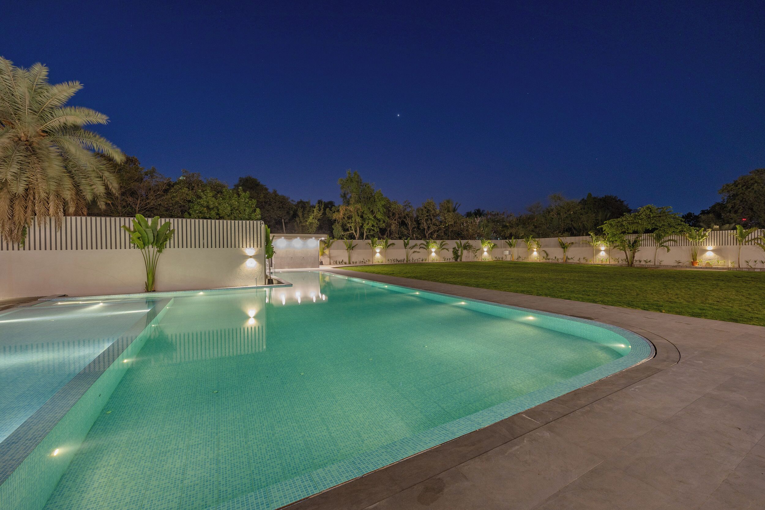 A swimming pool with a tiled edge, surrounded by a low wall and a grassy area.