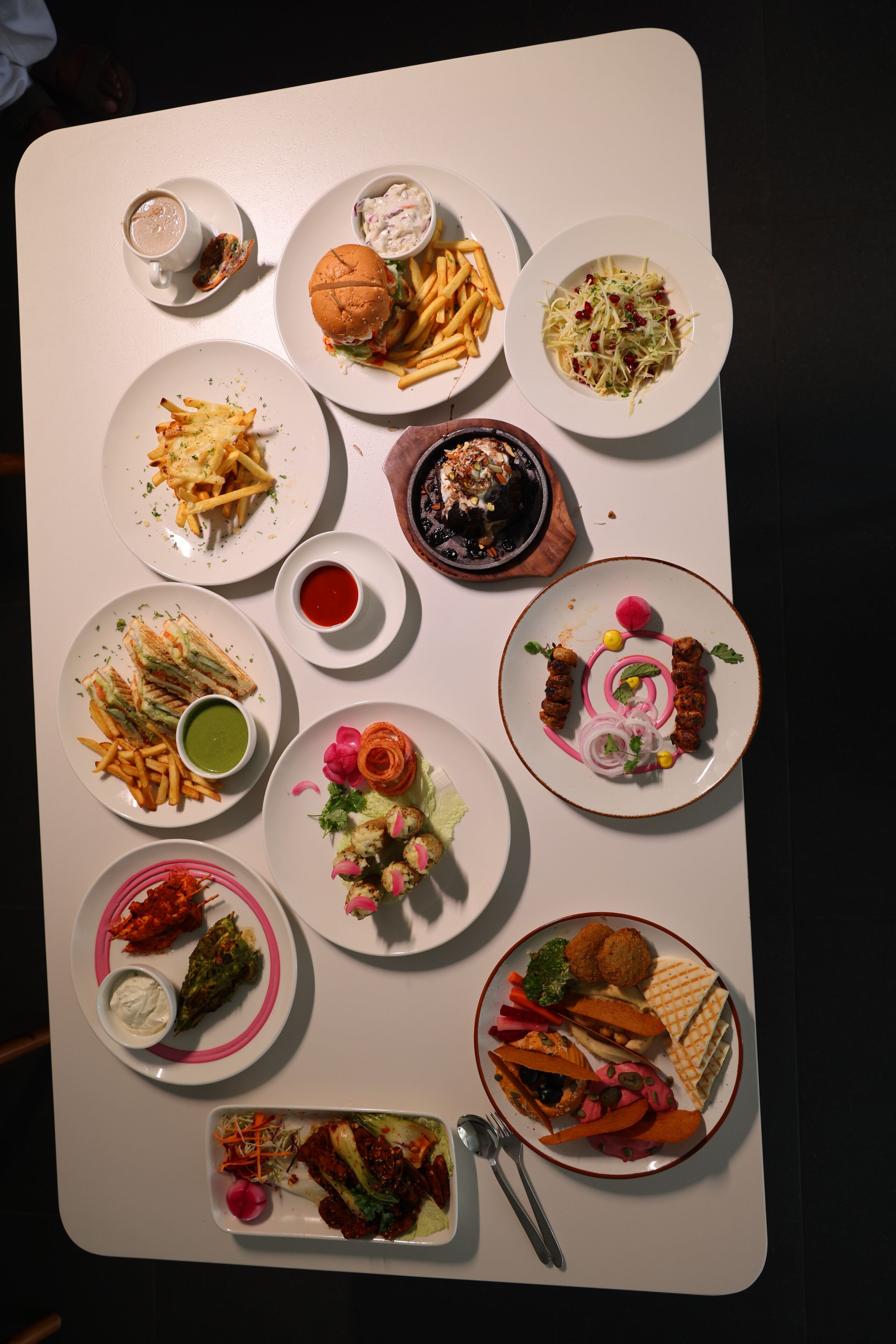 Una mesa con diversos platos, incluyendo una hamburguesa, papas fritas, ensalada y otros productos.