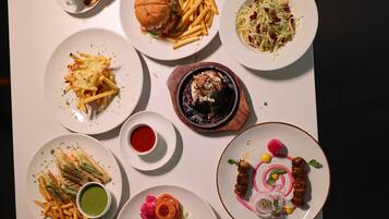 Una mesa con diversos platos, incluyendo una hamburguesa, papas fritas, ensalada y otros productos.