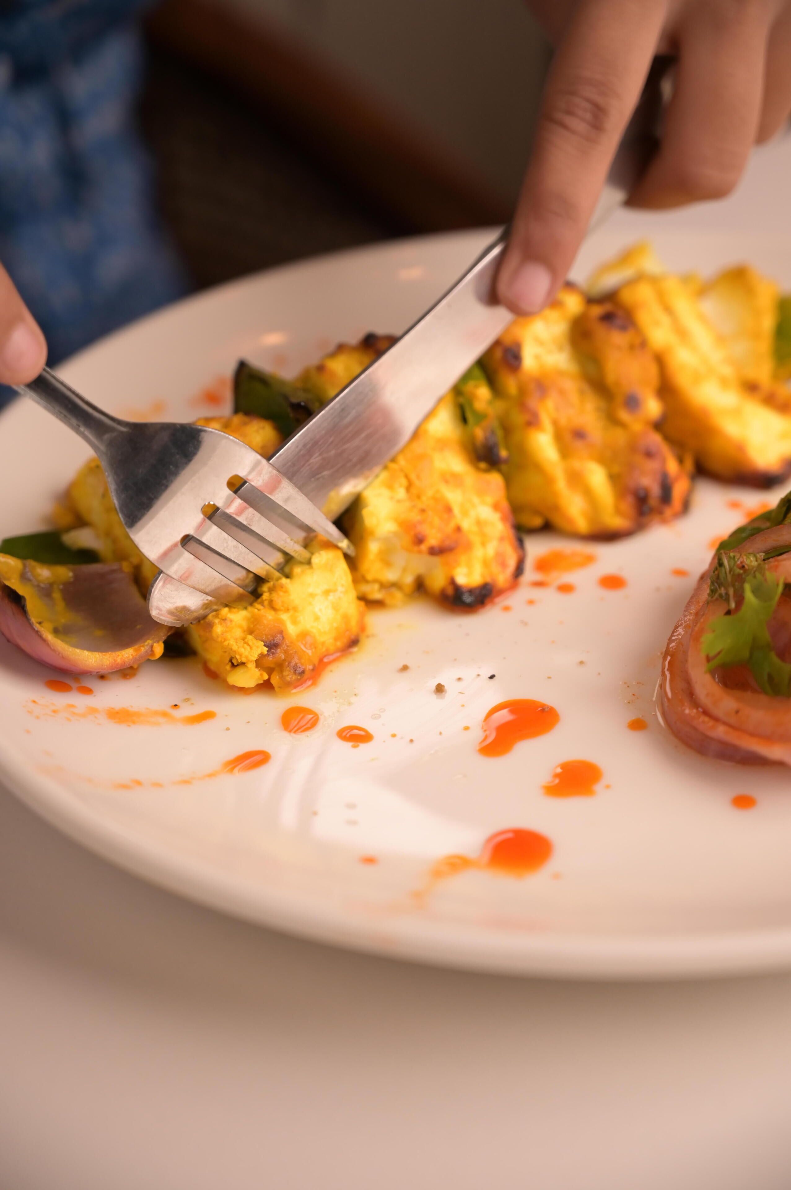 A person using a fork to eat a dish with a sauce on a white plate.