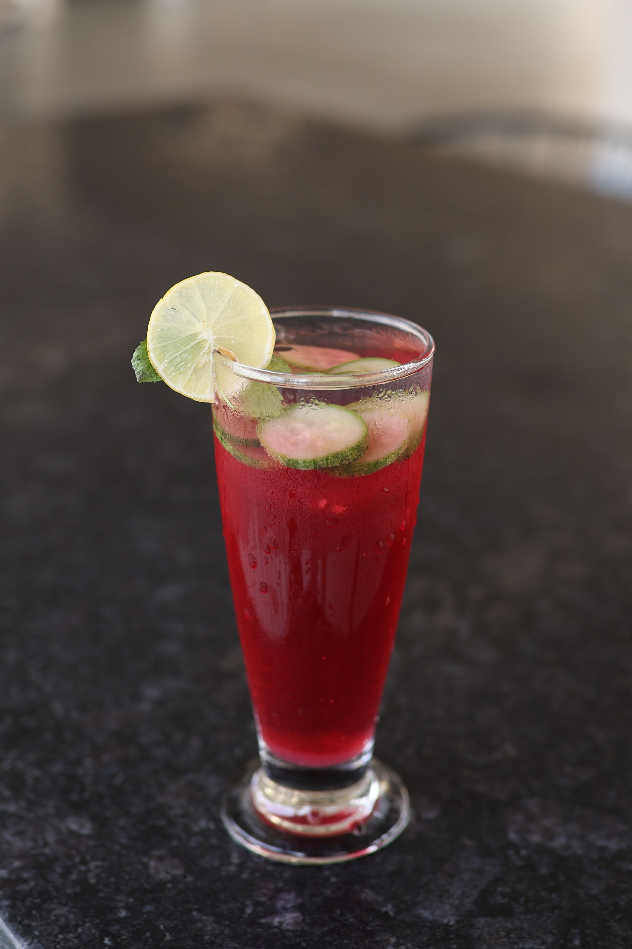 A tall glass with a red beverage, ice cubes, lime slice, and mint leaves.